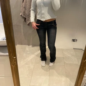 Mörkblå jeans med detaljer - Snygga mörkblå jeans med låg midja och bootcut-stil. Byxorna har dekorativa knappar och sömmar vid fickorna, vilket ger en unik touch. Perfekta för en avslappnad look.