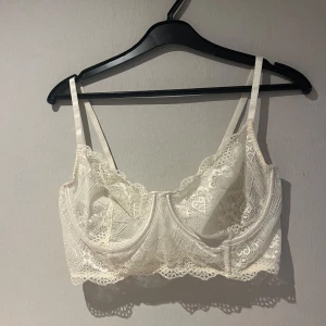 Vit spetskorsett - Elegant vit korsett med spetsdetaljer och justerbara axelband. Den har en vacker spetsdesign och hakknäppning bak för en perfekt passform.