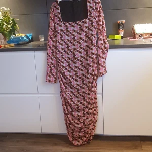 Mönstrad långklänning från Gina Tricot - Snygg långklänning från Gina Tricot med geometriskt mönster i rosa, svart och beige. Klänningen har långa ärmar och en fyrkantig halsringning, perfekt för en stilfull look. Drapering längst ner.