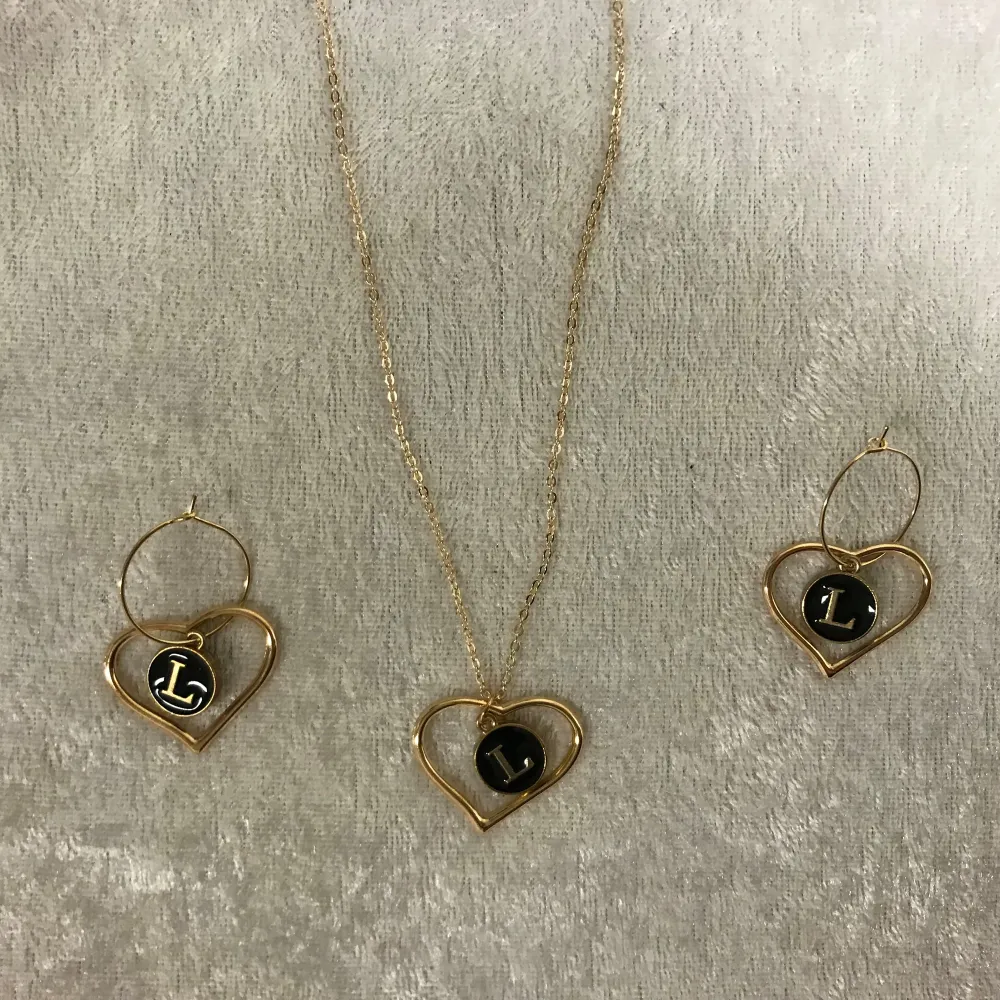 Elegant smyckesset med ett halsband och matchande örhängen i guld. Varje smycke har ett hjärta med en svart platta och en bokstav i mitten. Perfekt för att ge en personlig touch till din stil. Finns A-Z kvar , 139kr / set /paket. Justerbar halsband lång helt ny . Asusteet.