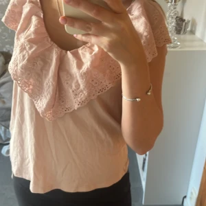 Rosa blus med spetsdetaljer - Söt rosa blus med en stor spetskrage. Perfekt för en romantisk look. Blusen har korta ärmar och en lös passform.