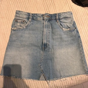 Jeanskjol från Authentic Denim ZARA - Snygg jeanskjol från Authentic Denim med en klassisk blå tvätt. Kjolen har en rå kant nertill och slitna detaljer vid fickorna. Perfekt för en avslappnad stil.