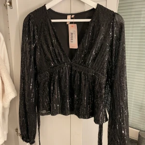 Sequin tie top från Nelly - Svart glittrig topp från Nelly💗 Helt oanvänd med prislappen kvar!! För tillfället slut på hemsidan vad jag vet