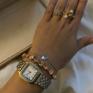 Silverfärgad klocka - Elegant silverfärgad klocka med fyrkantig urtavla och gnistrande stenar runt boetten. Armbandet är i rostfritt stål med justerbara länkar. Perfekt för att ge en stilren touch till din outfit. Från Ivy n Rox 