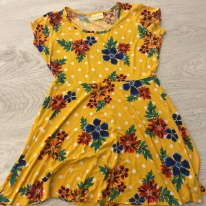 Gul blommig klänning från Bobbie Brooks - Charmig gul klänning med blommigt mönster och vita prickar från Bobbie Brooks. Den har korta ärmar och en rund halsringning, perfekt för en färgglad look.