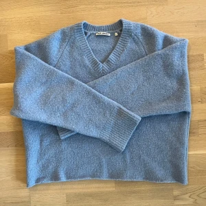 Blå stickad tröja från Our Legacy - Mysig blå stickad tröja från Our Legacy med v-ringning. Perfekt för kyligare dagar. Tröjan har långa ärmar och ribbade kanter som ger en stilren look.