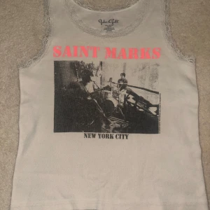 Vit ärmlös topp från John Galt - Säljer en vit ärmlös topp från John Galt med tryck av 'Saint Marks New York City' i rosa och svart. Toppen har spetsdetaljer runt ärmhålen och halsen. Perfekt för en avslappnad stil!