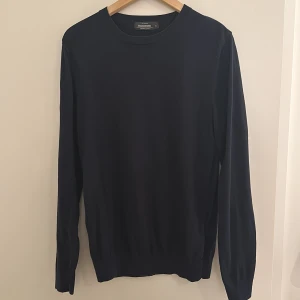 Marinblå tröja från Dressmann - Säljer en stilren marinblå tröja från Dressmann i bomull. Tröjan har långa ärmar och en klassisk rund halsringning. Perfekt för en enkel och elegant look. Passar bra till både jeans och chinos, 9/10 i skick. Pris kan diskuteras 