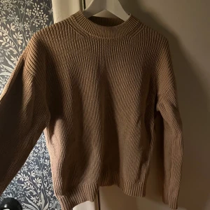 Beige stickad tröja - Säljer en stilren beige stickad tröja med rund halsringning. Tröjan har långa ärmar och ribbade kanter vid ärmslut och nederkant. Perfekt för kyligare dagar!