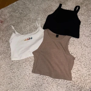 Tre linnen i olika färger - Säljer tre snygga linnen i olika färger. Ett ribbat beige linne, ett vitt linne med färgglada yin-yang-symboler och ett enkelt svart linne. Perfekta för sommaren och kan matchas med olika outfits.