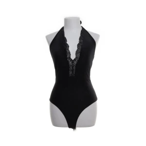 Svart body från Bik Bok - Snygg svart body från Bik Bok med djup v-ringning och spetsdetaljer. Den har en ribbad textur och knytning i nacken för en justerbar passform. Säljer då jag köpte den för en specifik sak och den inte kommer användas något mer.