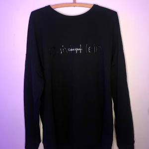 Svart långärmad tröja från Calvin Klein - Snygg svart långärmad tröja från Calvin Klein med logga på bröstet. Perfekt för en stilren look. Tröjan är i en klassisk design och passar till många olika outfits.