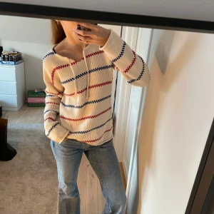 Mysig stickad kärringötröja  - Säljer en snygg stickad tröja från emmamalena i vit med röda och blå ränder som aldrig är använd. Tröjan har en avslappnad passform med långa ärmar och en dragsko vid halsen. Perfekt för en casual look! Nypris 1000kr! 