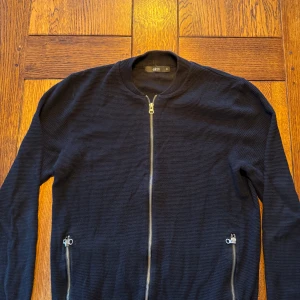 Svart zip up från ellos - Snygg svart Zip up från Ellos med dragkedja framtill och två fickor med dragkedjor. Jackan har en stilren design och är perfekt för en casual look. Den är långärmad och har en ribbad krage.