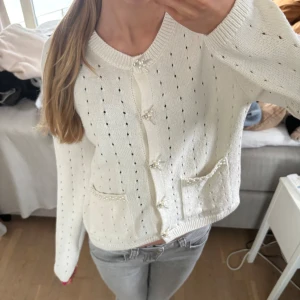Vit stickad kofta med pärldetaljer - Säljer en söt vit stickad kofta med pärldetaljer på knapparna och fickorna från Zara. Koftan har ett diskret hålmönster och långa ärmar. Perfekt för en stilren och elegant look, strl s❣️