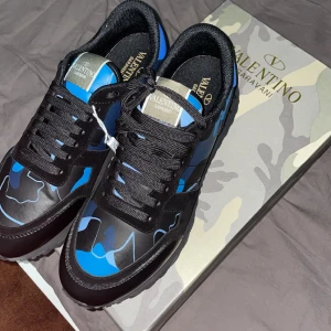 Valentino Rockrunner i blått och svart - Snygga Valentino Rockrunner sneakers i en cool blå och svart camouflage-design. Skorna har svarta snören och en robust sula, perfekt för en stilren look. Finns kvitto till dom