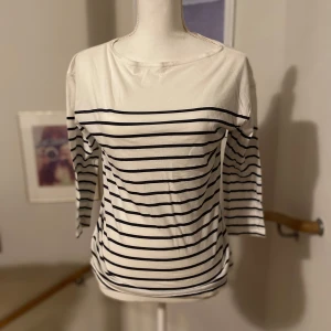 Vit och svart randig topp från Zara - Säljer en stilren vit och svart randig topp från Zara. Toppen har trekvartsärmar och en klassisk design som passar perfekt till vardags. Gjord i mjukt bomullsmaterial för extra komfort. Perfekt för en avslappnad look!