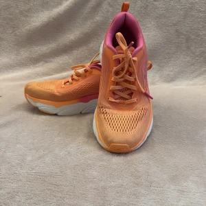 Orange och rosa sneakers - Snygga och färgglada sneakers i orange och rosa med vit sula. Skorna har snörning och en bekväm passform, perfekt för en aktiv livsstil. De har en modern design med ventilerande meshmaterial.Model Skecher go run. är som nya!
