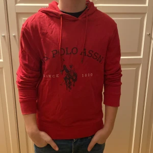 Röd hoodie från U.S. Polo Assn. - Säljer en snygg röd hoodie från U.S. Polo Assn. med tryck framtill. Den har en justerbar huva med snören och långa ärmar. Perfekt för en avslappnad stil. Den är xxs men passar xs 