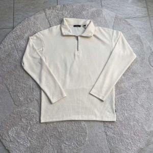 Vit långärmad tröja från Jack & Jones - Säljer en stilren vit långärmad tröja från Jack & Jones. Tröjan har en dragkedja vid halsen och är tillverkad i ett ribbat material. Perfekt för en avslappnad och snygg look.