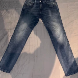 Blå jeansbyxor - Snygga blå Replay jeansbyxor med en klassisk straight passform. Modellen på jeansen är Anbass. De har en midwaist design och är perfekta för en avslappnad stil. Byxorna har fem fickor och stängs med dragkedja och knapp.