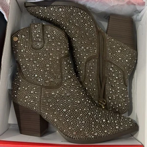 Brun/gröna boots med glittriga detaljer - Snygga bruna/gröna boots med glittriga detaljer och dragkedja på sidan. De har en bred klack och spetsig tå, vilket ger dem en elegant look. Perfekta för att sätta lite extra stil på din outfit och använda till exempel cowboy inspirerad fest:) aldrig använda