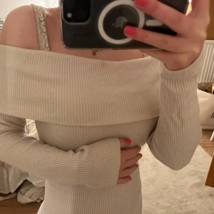 Beige offshoulder ribbad tröja - Säljer en stilren beige offshoulder tröja med ribbad struktur. Tröjan har långa ärmar och en elegant passform som framhäver axlarna. Perfekt för en trendig look.