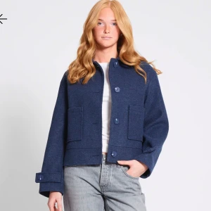 Mörkblå ulljacka - Snygg mörkblå ulljacka med stora knappar och fickor framtill. Jackan har en klassisk design med långa ärmar och en rak passform. Perfekt för kyligare dagar.