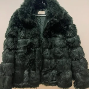 Mörkgrön pälsjacka - Säljer en lyxig mörkgrön pälsjacka med en fluffig och mjuk textur. Jackan har en klassisk design med långa ärmar och en bekväm passform. Perfekt för att hålla sig varm och stilren under kyliga dagar.