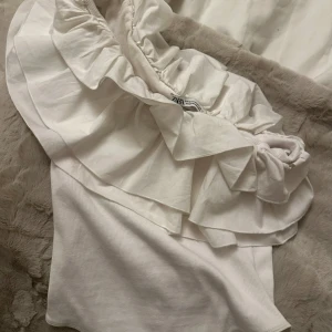 Vit offshoulder topp med volang - Säljer en söt vit offshoulder body från Zara med volangdetaljer. Använd en gång💕storlek m men passar s 