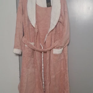 Rosa morgonrock från Line - Mysig rosa morgonrock från Line med vit fluffig krage och muddar. Den har ett knytband i midjan och är perfekt för att hålla sig varm och bekväm hemma. 💖