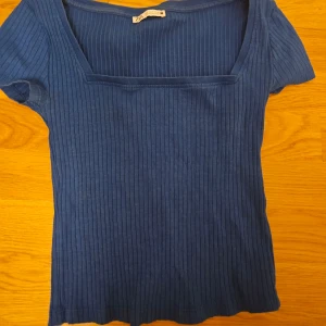Blå ribbad topp från Zara - Säljer en snygg blå ribbad topp från Zara. Toppen har korta ärmar och en fyrkantig halsringning som ger en stilren look. Perfekt för en avslappnad stil.