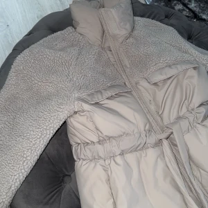 Jacka   - Säljer en snygg och populär beige teddyjacka . Jackan har en hög krage och ett bälte i midjan för en justerbar passform. Jackan är slutsåld och inte använd mycket storlek xs men passar även S/M beroende på hur man vill att den ska sitta 