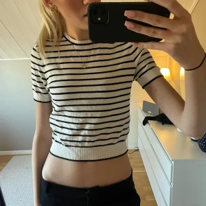 Randig kortärmad topp från H&M - Säljer en snygg randig topp från H&M i svart och vit. Den har korta ärmar och en ribbad kant vid ärmslut och nederkant. Perfekt för en stilren look! Endast använd 1 gång.