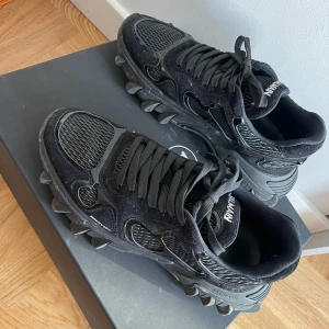 Svarta sneakers från Balmain - Snygga svarta sneakers från Balmain med unik sula och snörning. Skorna är tillverkade i en kombination av mocka och mesh, vilket ger en stilren och modern look. Perfekta för dig som vill ha något extra i garderoben.