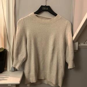Beige stickad tröja från  Veramoda  - Mysig beige stickad tröja från veramoda med trekvartsärm och rund hals. Perfekt för kyligare dagar med sin mjuka och bekväma passform. En stilren och enkel design som passar till många tillfällen.