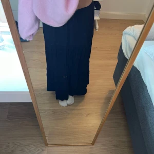 Svart långkjol - Är 167 och kjolen är lite kort på mig. Säljer en stilren svart långkjol med volanger. Kjolen har en lös passform och är perfekt för både vardag och speciella tillfällen. Den är tillverkad i ett mjukt och bekvämt material som faller fint.