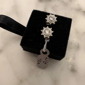Silverfärgade örhängen med glittriga stenar - Snygga silverfärgade örhängen med en glittrig sten i mitten omgiven av små detaljer. Perfekta för att ge en extra touch till din outfit. Nya ej använda äkta silver 925