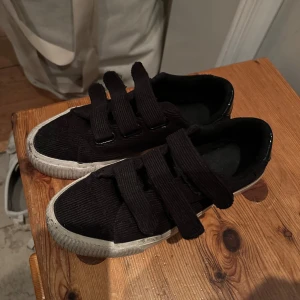 Svarta sneakers med kardborreband - Snygga svarta sneakers med breda kardborreband och en vit sula. Skorna har en unik textur som ger dem en cool look. Perfekta för en avslappnad stil.
