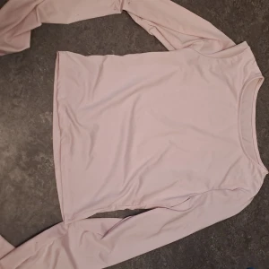 Ljusrosa långärmad topp - Säljer en söt ljusrosa långärmad topp. Perfekt för en avslappnad stil och kan matchas med olika outfits. Toppen har en enkel design med rund halsringning. Materialet känns lite som en  träningströja. Fler tröjor medföljer