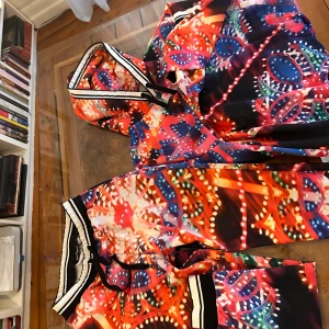 Färgglada byxor och hoodie  från Dolce & Gabbana - Säljer ett par färgglada lounge/tränings byxor från Dolce & Gabbana med en hoodie till med ett unikt och livfullt mönster. Byxorna har en elastisk midja med snörning och svarta och vita ränder. Hoodie samma sak. Perfekta för dig som vill sticka ut med en färgsprakande stil.