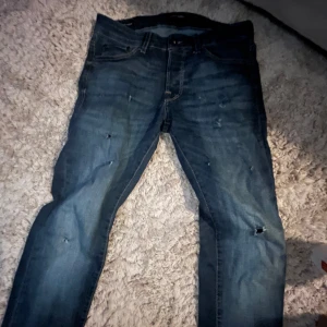 Jeans mörkblå - Snygga blå jeans från Jack & Jones med slitna detaljer. De har en klassisk femficksdesign och stängs med dragkedja och knapp. Perfekta för en avslappnad stil.