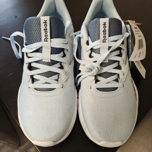 Ljusblå sneakers från Reebok - Snygga ljusblå sneakers från Reebok med vit sula och snörning. Perfekta för en sportig look. Tillverkade i syntetmaterial med en bekväm passform.