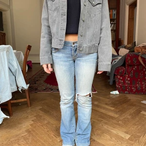 Blå bootcut jeans med slitningar - Snygga blå bootcut jeans med slitningar på knäna. De har en klassisk femficksdesign och en lågmidjad passform. Perfekta för en avslappnad stil. Köpta second hand! 