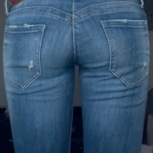 Lågmidjade jeans - Snygga blå jeans med slitningar och en klassisk femficksdesign. De har en knapp och dragkedja framtill. Perfekta för en avslappnad stil.