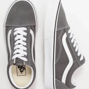 Grå sneakers från Vans - Snygga grå sneakers från Vans med klassisk vit sidosymbol och snörning. Perfekta för en avslappnad stil. Skorna har en vit sula och är tillverkade i ett slitstarkt material.