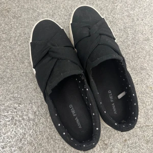 Svarta sneakers från Anna Field - Snygga svarta sneakers från Anna Field med en unik knytdetalj på ovansidan. Skorna har en vit sula och prickigt mönster på insidan. Perfekta för en stilren och bekväm look.
