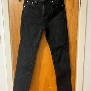 Svarta jeansbyxor - Snygga svarta jeansbyxor med hög midja och en tight passform. Klassisk design med fem fickor och knappgylf. Perfekta för en stilren look.