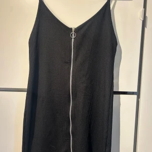 Svart ribbad klänning från Bershka - Snygg svart kort ribbad klänning från Bershka med dragkedja framtill. Klänningen har smala axelband och en figurnära passform.