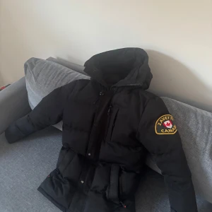 Svart dunjacka från Zavetti Canada - Snygg och praktisk jacka från Zanetti Canada i storlek XS, i mycket bra och fräscht skick. Denna jacka är perfekt för vinterkylan och har en avtagbar päls som ger dig möjlighet att anpassa stilen efter vädret. Med sin stiliga design och funktionalitet är den ett utmärkt val för både vardag och fritid. Missa in